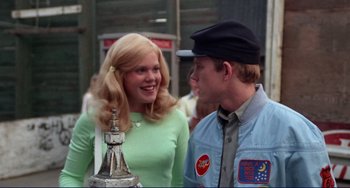 Movie still from “Eat My Dust” (1976), directed by Charles B. Griffith – A man and a woman standing next to each other on the street; Medium shot, Over the shoulder angle