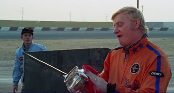 Movie still from “Eat My Dust” (1976), directed by Charles B. Griffith – A man in an orange and blue jacket holding a metal container; Medium shot, Low angle
