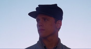 Movie still from “Eat My Dust” (1976), directed by Charles B. Griffith – A young man wearing a hat looking up at the sky; Close Up shot, Low angle