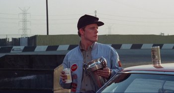 Movie still from “Eat My Dust” (1976), directed by Charles B. Griffith – A man standing next to a car holding a cup and tea pot; Medium shot, Low angle