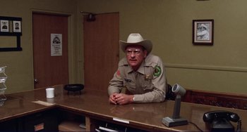 Movie still from “Eat My Dust” (1976), directed by Charles B. Griffith – A man sitting at a table wearing a cowboy hat; Medium shot, Over the shoulder angle
