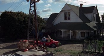 Movie still from “Eat My Dust” (1976), directed by Charles B. Griffith – Two people sitting in a red car in front of a house; Extreme Wide shot, High angle