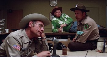 Movie still from “Eat My Dust” (1976), directed by Charles B. Griffith – A group of men sitting around a table; Wide shot, Low angle