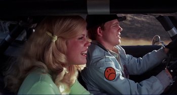 Movie still from “Eat My Dust” (1976), directed by Charles B. Griffith – A man and a woman riding in the back of a car; Close Up shot, Low angle
