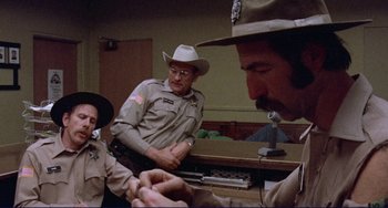 Movie still from “Eat My Dust” (1976), directed by Charles B. Griffith – A group of men sitting around a table; Medium shot, Over the shoulder angle