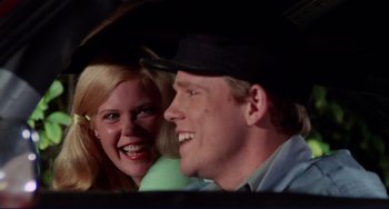 Movie still from “Eat My Dust” (1976), directed by Charles B. Griffith – A man and a woman smiling for the camera; Close Up shot, Over the shoulder angle