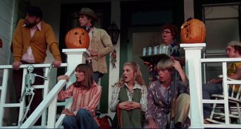 Movie still from “Eat My Dust” (1976), directed by Charles B. Griffith – A group of people sitting on a porch with a pumpkin; Wide shot, High angle