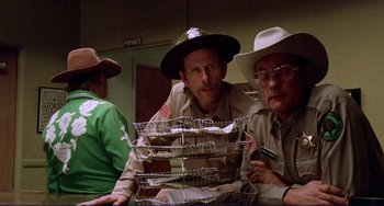 Movie still from “Eat My Dust” (1976), directed by Charles B. Griffith – A group of men standing next to each other in a room; Medium shot, Over the shoulder angle