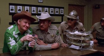 Movie still from “Eat My Dust” (1976), directed by Charles B. Griffith – A group of men sitting at a table; Medium shot, Over the shoulder angle
