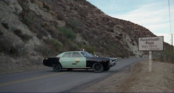 Movie still from “Eat My Dust” (1976), directed by Charles B. Griffith – An old police car driving down a road; Wide shot, Low angle