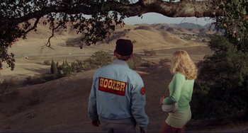 Movie still from “Eat My Dust” (1976), directed by Charles B. Griffith – A man and a woman standing on top of a hill; Wide shot, High angle