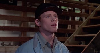 Movie still from “Eat My Dust” (1976), directed by Charles B. Griffith – A man wearing a baseball cap and a blue shirt; Close Up shot, Over the shoulder angle