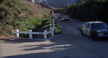 Movie still from “Eat My Dust” (1976), directed by Charles B. Griffith – A group of cars driving down a road next to trees; Extreme Wide shot, High angle