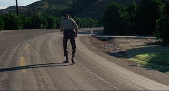Movie still from “Eat My Dust” (1976), directed by Charles B. Griffith – A man riding a skateboard down the side of a dirt road; Wide shot, Low angle