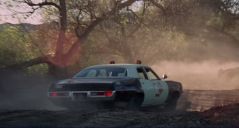 Movie still from “Eat My Dust” (1976), directed by Charles B. Griffith – A police car driving on a dirt road near a forest; Wide shot, Low angle