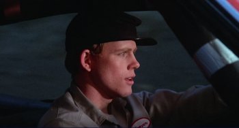 Movie still from “Eat My Dust” (1976), directed by Charles B. Griffith – A man wearing a hat sitting in the drivers seat of a car; Close Up shot, Low angle