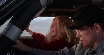 Movie still from “Eat My Dust” (1976), directed by Charles B. Griffith – A woman in a red shirt is driving a car; Close Up shot, Low angle