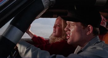 Movie still from “Eat My Dust” (1976), directed by Charles B. Griffith – A man and a woman in the driver's seat of a car; Close Up shot, Low angle