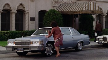 Movie still from “Eating Raoul” (1982), directed by Paul Bartel – A woman in a short skirt standing in front of a car; Wide shot, Low angle