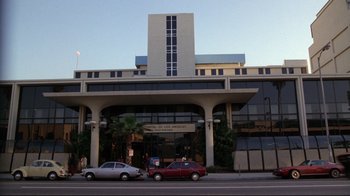 Movie still from “Eating Raoul” (1982), directed by Paul Bartel – Two cars parked on the side of the road near a building; Extreme Wide shot, Low angle