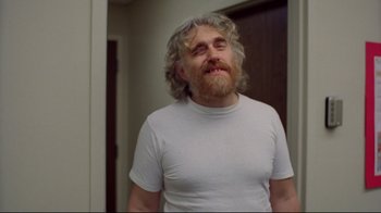 Movie still from “Eating Raoul” (1982), directed by Paul Bartel – A man with long hair and a white shirt is standing in front of a mirror; Close Up shot, Low angle