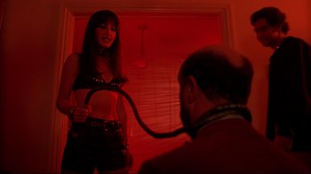 Movie still from “Eating Raoul” (1982), directed by Paul Bartel – A woman in a leather outfit is holding a whip; Medium shot, Over the shoulder angle