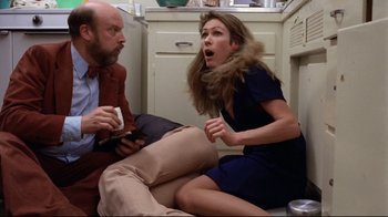 Movie still from “Eating Raoul” (1982), directed by Paul Bartel – A woman in a blue dress is sitting on the floor with a man in a brown suit; Medium shot, Low angle