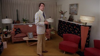 Movie still from “Eating Raoul” (1982), directed by Paul Bartel – A man standing in a living room holding a lamp; Wide shot, Over the shoulder angle