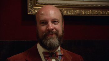 Movie still from “Eating Raoul” (1982), directed by Paul Bartel – A man with a beard wearing a suit and bow tie; Close Up shot, Low angle