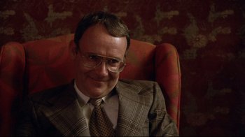 Movie still from “Eating Raoul” (1982), directed by Paul Bartel – A man sitting in a chair wearing a suit; Close Up shot, Low angle