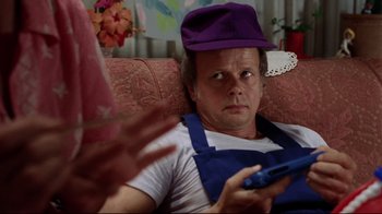 Movie still from “Eating Raoul” (1982), directed by Paul Bartel – A man wearing a purple hat holding a remote control; Close Up shot, Over the shoulder angle