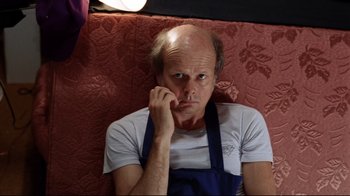 Movie still from “Eating Raoul” (1982), directed by Paul Bartel – A man with an apron is sitting on a couch; Close Up shot, High angle