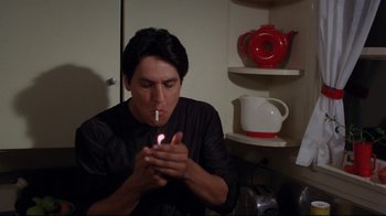 Movie still from “Eating Raoul” (1982), directed by Paul Bartel – A man is lighting a cigarette in a kitchen; Medium shot, High angle