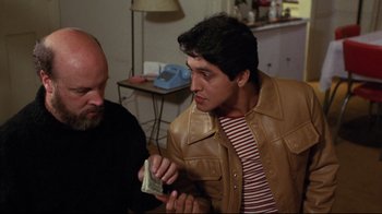 Movie still from “Eating Raoul” (1982), directed by Paul Bartel – A man in a brown leather jacket holding a stack of money; Medium shot, Over the shoulder angle