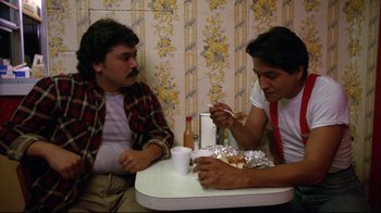 Movie still from “Eating Raoul” (1982), directed by Paul Bartel – Two men sitting at a table eating food; Medium shot, High angle