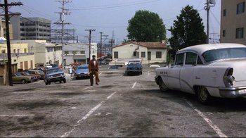 Movie still from “Eating Raoul” (1982), directed by Paul Bartel – A man walking across a parking lot next to cars; Wide shot, High angle