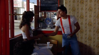 Movie still from “Eating Raoul” (1982), directed by Paul Bartel – A man and a woman are shaking hands in front of a table; Medium shot, Over the shoulder angle