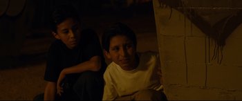 Movie still from “El Chicano” (2018), directed by Ben Hernandez Bray – Two young boys sitting on the ground in a dark room; Medium shot, High angle