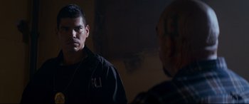 Movie still from “El Chicano” (2018), directed by Ben Hernandez Bray – A man standing next to another man in a dark room; Medium shot, Over the shoulder angle
