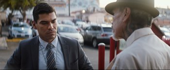 Movie still from “El Chicano” (2018), directed by Ben Hernandez Bray – A man wearing a suit and tie talking to another man wearing a hat; Close Up shot, Over the shoulder angle