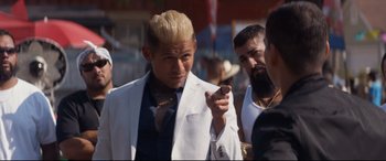 Movie still from “El Chicano” (2018), directed by Ben Hernandez Bray – A man in a white suit is pointing at something in his hand; Close Up shot, Over the shoulder angle