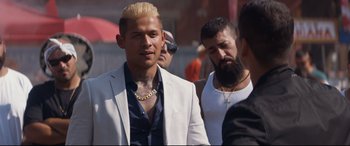 Movie still from “El Chicano” (2018), directed by Ben Hernandez Bray – A man in a white jacket and a gold chain necklace; Close Up shot, Over the shoulder angle