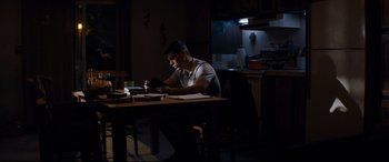 Movie still from “El Chicano” (2018), directed by Ben Hernandez Bray – A man sitting at a table in the dark looking at papers; Medium shot, Low angle