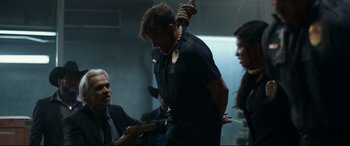 Movie still from “El Chicano” (2018), directed by Ben Hernandez Bray – A man is tied to a rope while two other people look on; Medium shot, Over the shoulder angle