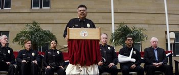 Movie still from “El Chicano” (2018), directed by Ben Hernandez Bray – A man is speaking at an event in front of a group of police officers; Medium shot, Low angle