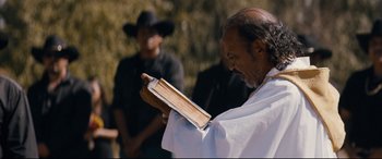Movie still from “El Chicano” (2018), directed by Ben Hernandez Bray – An older man reading a book while another man looks on; Medium shot, Over the shoulder angle