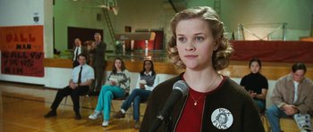 Movie still from “Election” (1999), directed by Alexander Payne – A woman standing in front of a microphone in front of a group of people; Close Up shot, Low angle