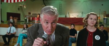 Movie still from “Election” (1999), directed by Alexander Payne – A man in a suit and tie holding a microphone in his hand; Close Up shot, Low angle