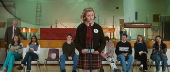 Movie still from “Election” (1999), directed by Alexander Payne – A woman standing at a microphone in front of a group of people; Medium shot, Low angle