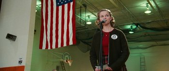 Movie still from “Election” (1999), directed by Alexander Payne – A woman standing in front of an american flag; Medium shot, Low angle